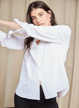 Load image into Gallery viewer, Woman in white shirt and black pants, showcasing the Connie Slim Button Down with a longer back hem and wrinkle-resistant Microfiber material.