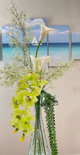 Load image into Gallery viewer, A beautiful vase with vibrant artificial Cymbidium orchids surrounded by real touch flowers and a serene ocean picture.
