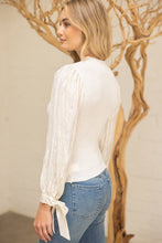 Load image into Gallery viewer, Woman wearing a white blouse and blue jeans standing against a neutral wall with wooden decor.
