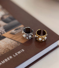 Load image into Gallery viewer, Two ornate rings, one gold and one silver, on a book titled 'Amber Lewis'.
