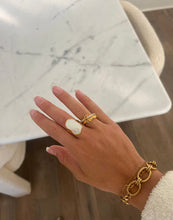 Load image into Gallery viewer, A gold ring featuring an irregular, lustrous white mother-of-pearl stone set atop, displayed on a smooth gray surface, exuding elegance and luxury.
