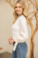 Load image into Gallery viewer, Woman wearing a white blouse and blue jeans standing in front of a decorative tree.
