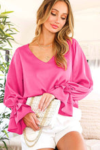 Load image into Gallery viewer, Woman wearing a bright pink blouse with long sleeves and white shorts, holding a clutch.
