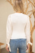 Load image into Gallery viewer, Person wearing a white blouse with long sleeves and blue jeans, standing in front of a decorative tree.
